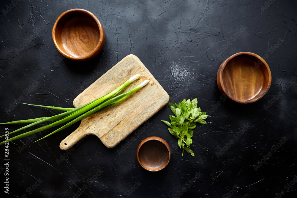 Cooking dinner. Cutting board and herb ingredients. Fresh mint leaves, scallion (green onion), empty natural wooden bowls on stone table, black background, top view, flat lay - obrazy, fototapety, plakaty 