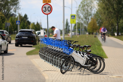 Rowery, mężczyzna przy stacji wypożyczania rowerów przy drodze, samochody i rowerzyści.