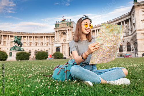 Canvas Print Happy asian woman traveler with map sitting on a green lawn in Vienna city