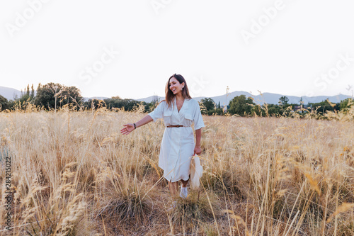 Fototapeta Naklejka Na Ścianę i Meble -  portrait of young beautiful caucasian woman outdoors walking at sunset in a yellow field. wearing a modern hat and smiling. Happiness concept