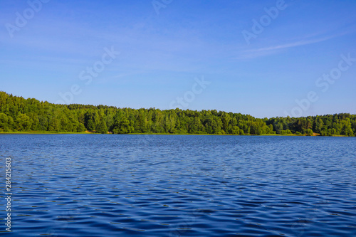 View of a blue lake or river on a sunny day on a background of blue sky and green forest.
