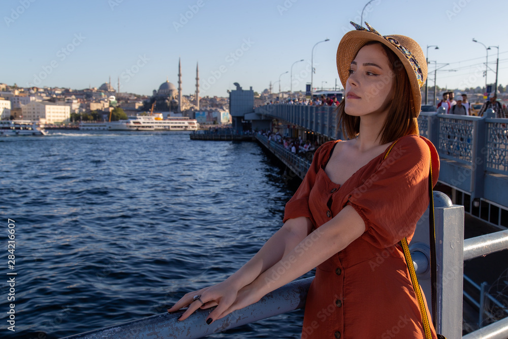 Beautiful girl with orange colored dress posing with the Galata Bridge and Mosques from Istanbul
