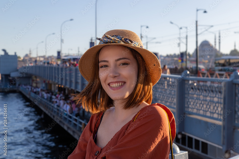 Beautiful girl with orange colored dress posing with the Galata Bridge and Mosques from Istanbul
