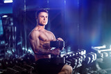 young adult man handsome athlete working out in gym, sitting on a bench and holding dumbbell with raised arms. indoor, looking weight.