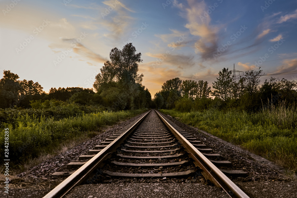 Fototapeta premium Railroad track through distant rural landscape at sunset