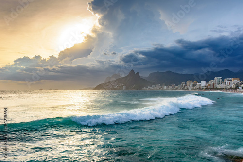Summer sunset with cloudy sky, surfers and citi view with Two Brothers hill and Vidigal slum view from Ipanema beach at Rio de Janeiro photo
