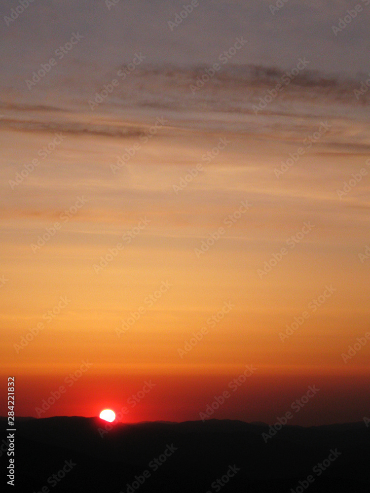 Sunrise in the mountains. Sunset sky. Nature photography orange clouds and sun over hill