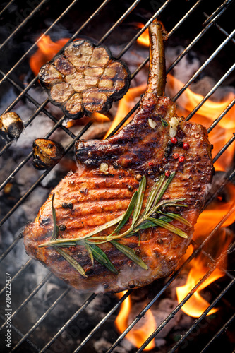 Bild auf Leinwand Grilled bone-in pork chop, pork steak, tomahawk in a rosemary-garlic marinade  on a flaming grill plate, close-up, top view