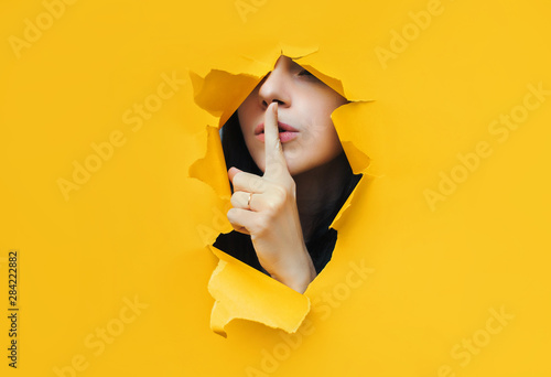 A young girl closes her lips with her index finger,making it clear to the viewer that you need to observe silence,keep a secret and not say too much. Censorship and harassment of freedom of speech. photo