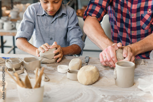 Cute caucasian boy making part of pots while his father kneading clay.