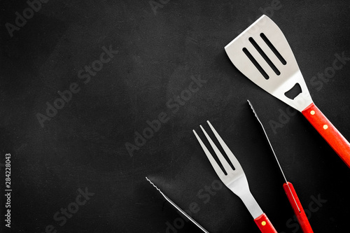 spatula, fork, tongs for barbecue on black background top view mock up