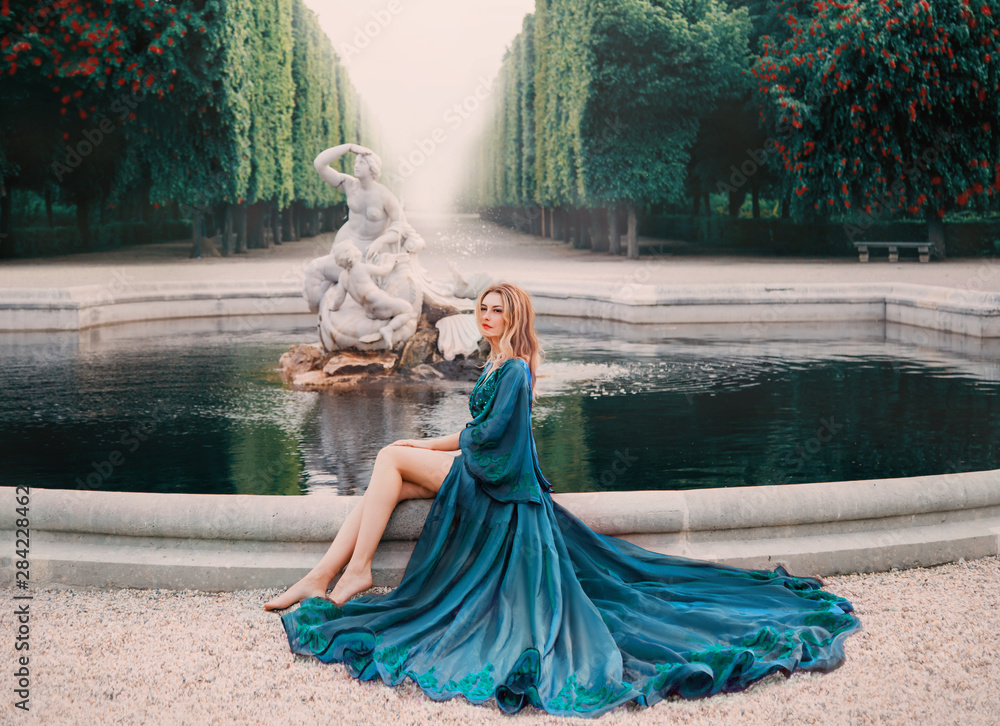 Φωτογραφία A young blonde woman sits near an old royal pond with ancient statues with a fountain and dreams