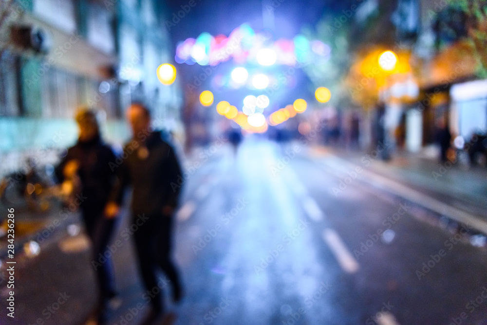 Urban night scene with people walking out of focus with colored background.