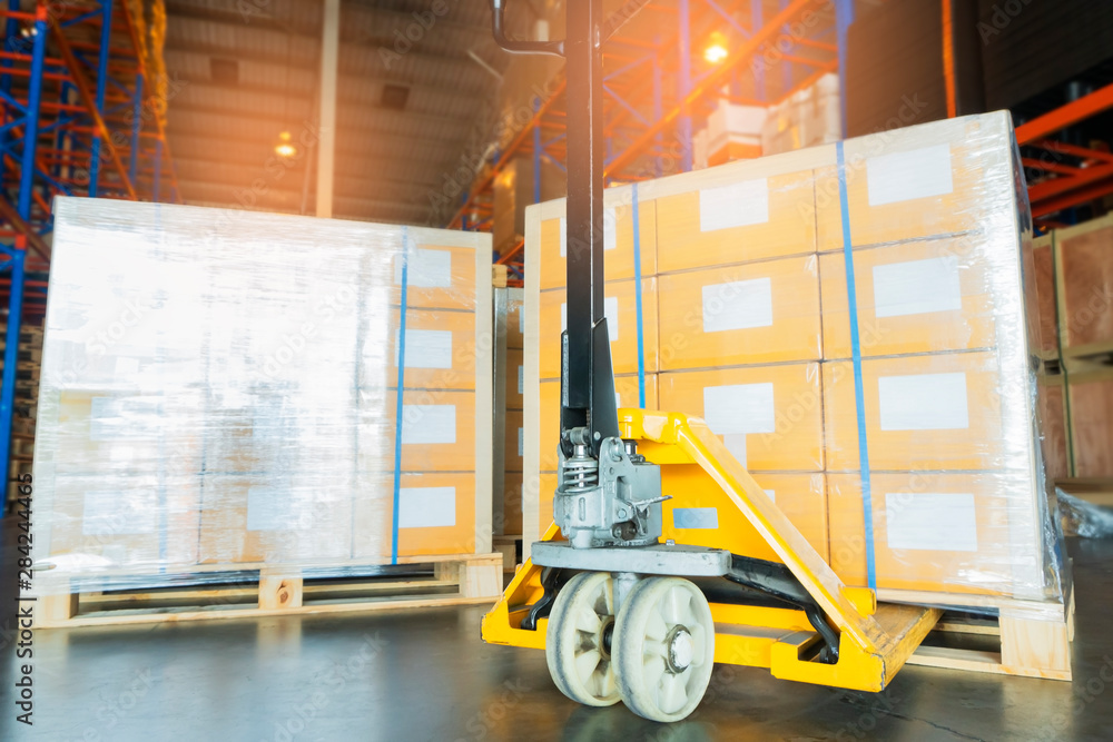 Naklejka premium hand pallet truck with stacked of package boxes on wooden pallet, cargo export for transportation at distribution warehouse.