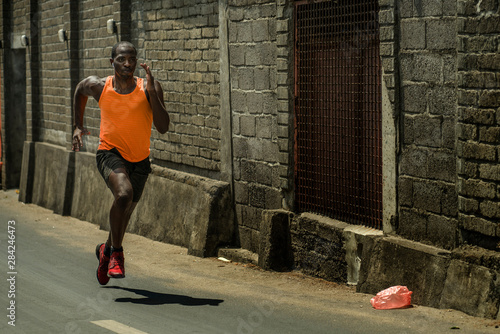 urban runner workout . Young attractive and athletic black afro American man running outdoors on asphalt road training hard jogging in sport and healthy lifestyle