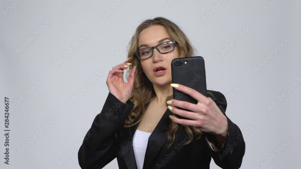 Pretty girl makes selfie on mobile phone then looking photos on gray background at studio Pretty girl makes selfie on mobile phone then looking photos on gray background at studio