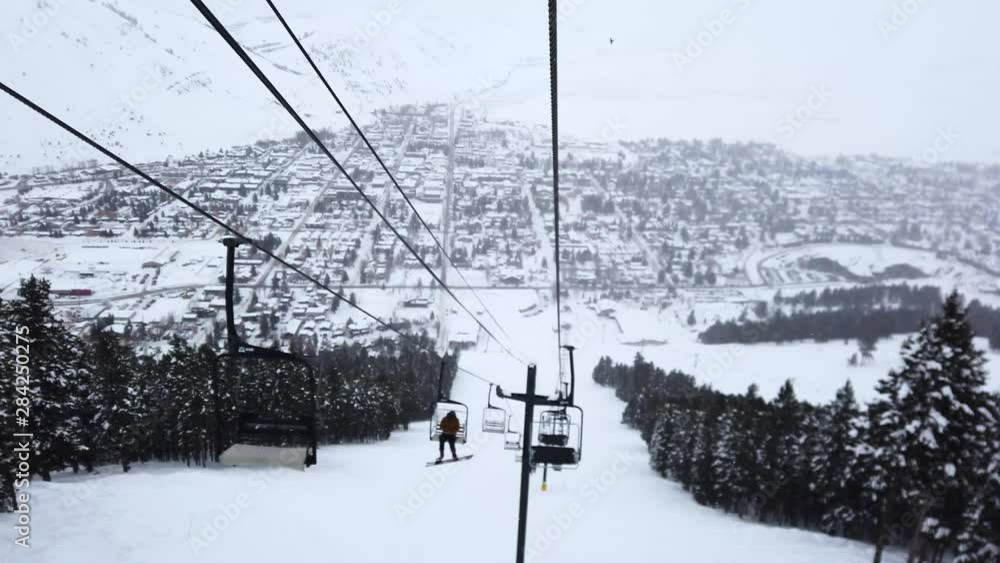 Snowboarder rides their way up the ski lift as the snow continues to fall and a eagle can be seen flying in the distance. Snowboarder rides their way up the ski lift as the snow continues to fall and a eagle can be seen flying in the distance.