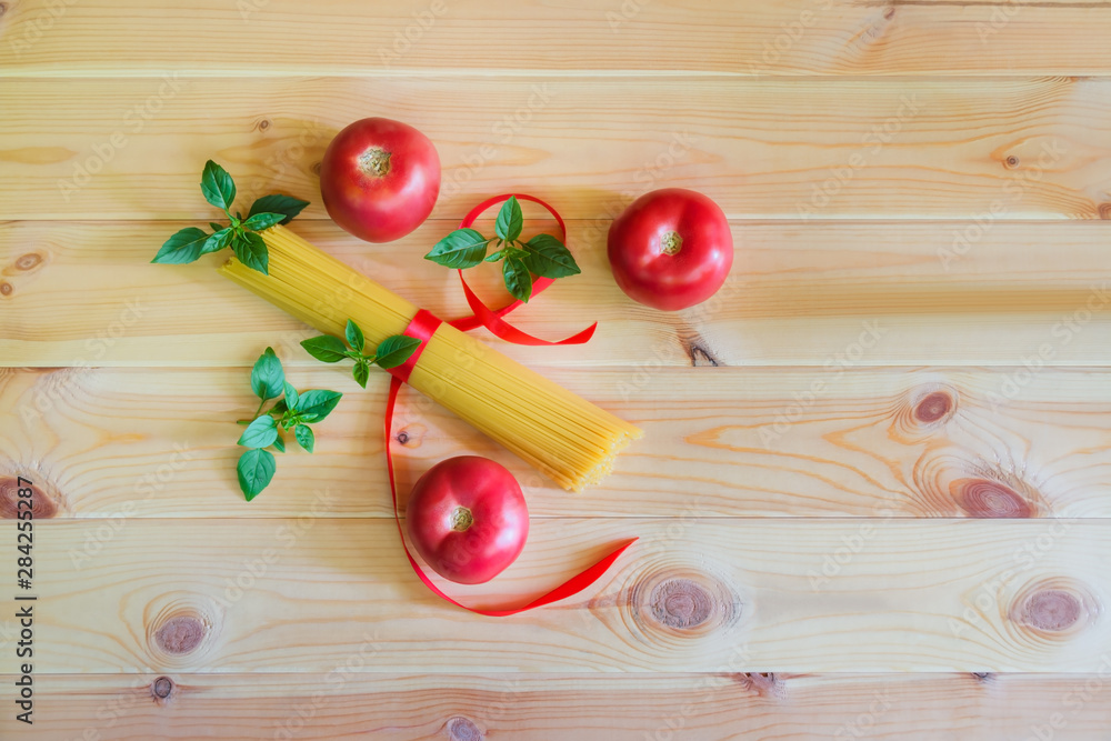 Raw spaghetti pasta with fresh tomatoes and basil leaves on wooden background. Top view, copy space. Raw spaghetti pasta with fresh tomatoes and basil leaves on wooden background. Top view, copy space.