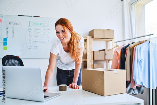 Young online business owner looking at laptop while preparing deliveries for clients photo