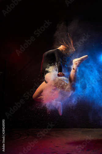 Young teen girl in a dark room during a photoshoot with flour with a colored light and a black background © keleny
