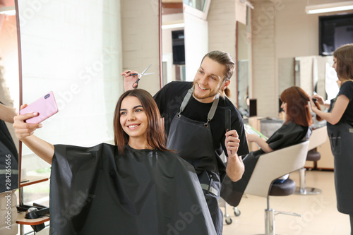 Young woman taking selfie with her hairdresser in salon