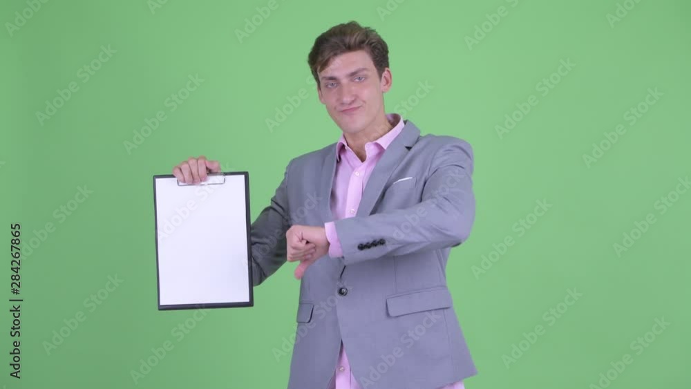 Stressed young businessman showing clipboard and giving thumbs down Stressed young businessman showing clipboard and giving thumbs down