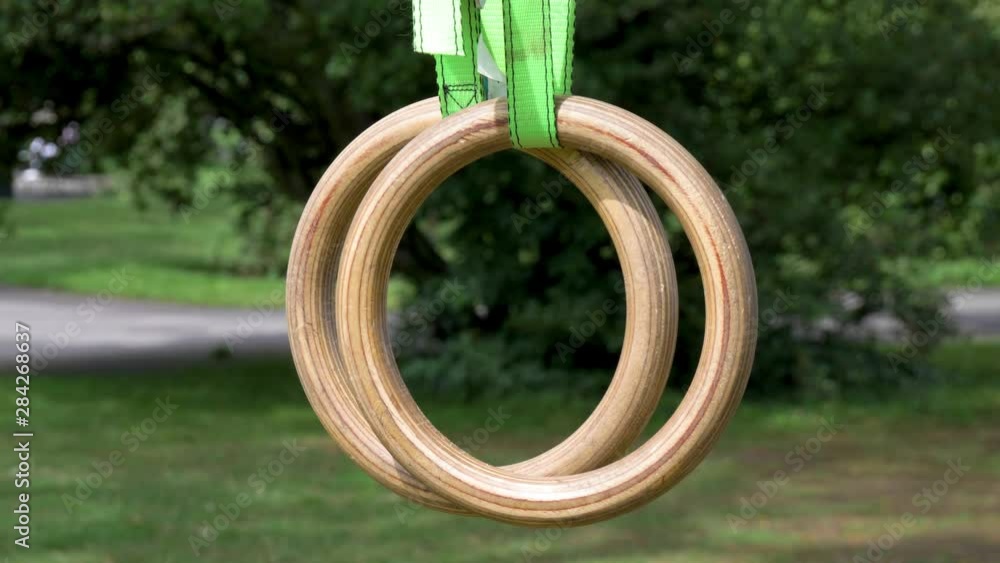 Crossfit and Gymnastic rings hanging from a tree in a park. The rings are in close up view suspended just in front of the camera and gently swaying. Crossfit and Gymnastic rings hanging from a tree in a park. The rings are in close up view suspended just in front of the camera and gently swaying.