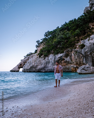 The beautiful bay in the Gulf of Orosei, Sardinia , young men walking in the evening on the beach photo