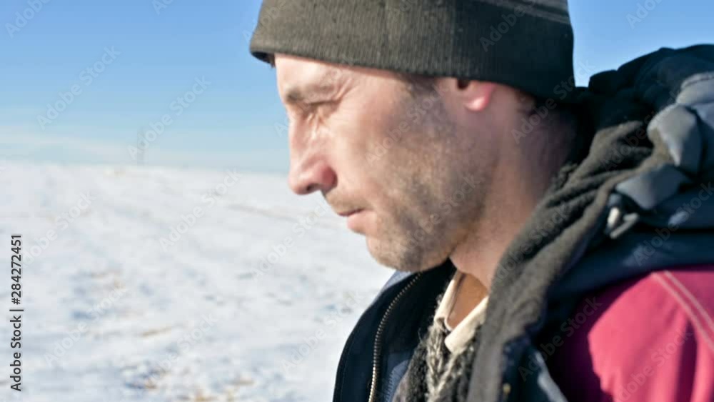 A Close-up portrait of a pensive man in a hat and a warm jacket on a sunny winter day in an outdoor field with snow-covered fields. Thoughtfully goes forward and looks at the tops A Close-up portrait of a pensive man in a hat and a warm jacket on a sunny winter day in an outdoor field with snow-covered fields. Thoughtfully goes forward and looks at the tops