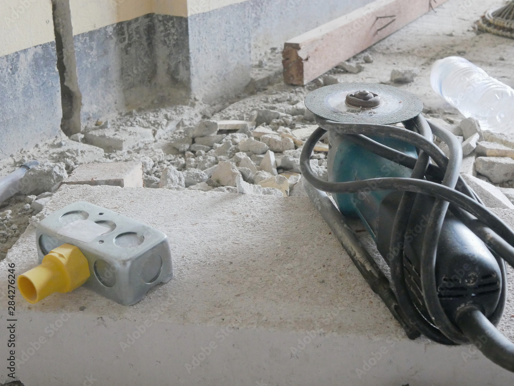 Old dusty angle grinder, with a diamond cutting disc, and an electrical back box placed on a lightweight concrete block after being used for running electrical wire in a house wall