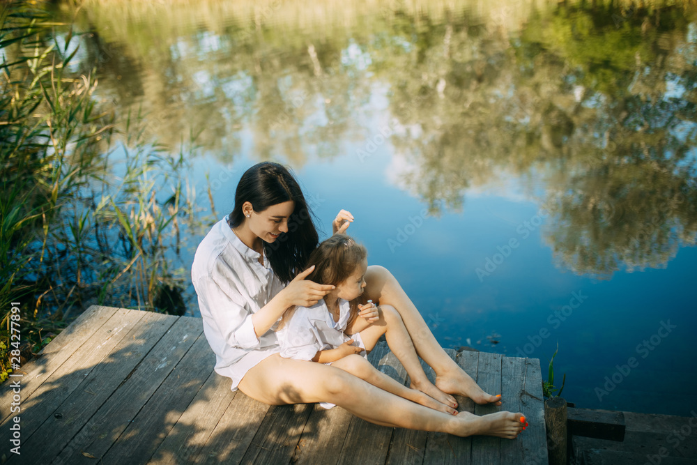 Mother and daughter are sitting on a wooden bridge over a river.