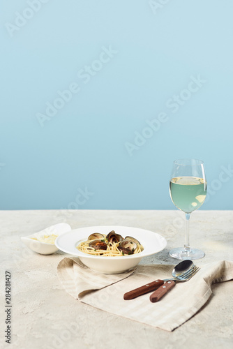 delicious Italian spaghetti with seafood served with white wine on napkin near cutlery isolated on blue