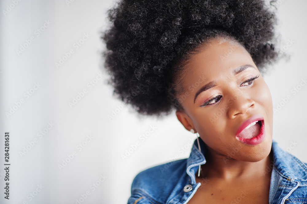 Close up portrait of an attractive african american woman with afro hair wear jeans jacket, posed at white room. Fashionable black model. Close up portrait of an attractive african american woman with afro hair wear jeans jacket, posed at white room. Fashionable black model.