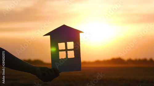 A woman's hand holds a paper house and passes it to a man's hand. House at sunset. The concept of family. Construction, mortgage and property sales. photo