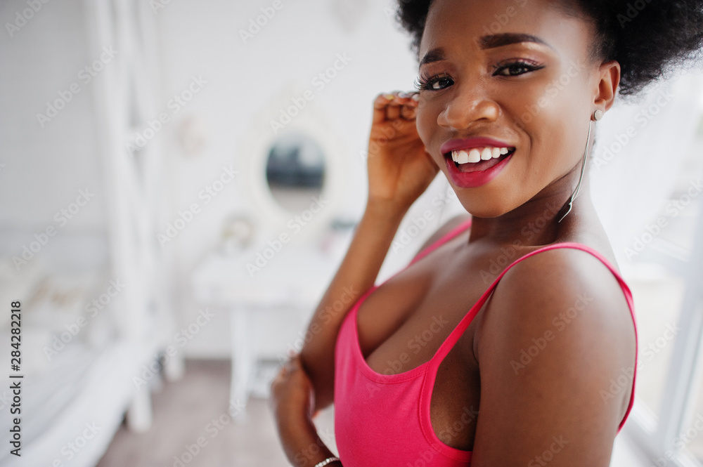 Attractive african american woman with afro hair wear on skirt pink top, posed at white room. Fashionable sexy black model. Attractive african american woman with afro hair wear on skirt pink top, posed at white room. Fashionable sexy black model.