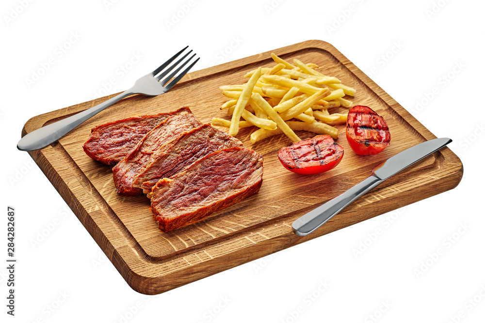Delicious medium rare steak with French fries and grilled cherry tomatoes on a cutting board with table knife and fork. Classic meat meal isolated on white background.
