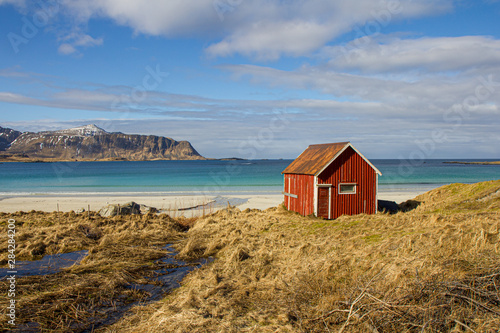 A typical red nordic hut at the seaside. Amazing and beautiful sunlit beach with mountain range in the background.