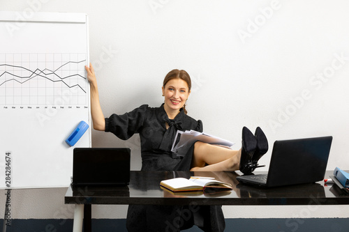 successful and joyful girl working in the office. the girl sitting at the table her feet on the table her hand she held a Board which is drawn work schedule. on the table two laptop and documents photo