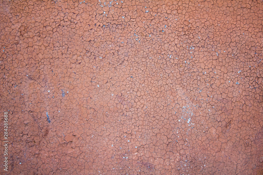 old concrete wall with cracks and peeling pink red paint. rough surface texture