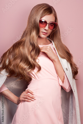 Young elegant woman in trendy white coat. Blond hair, pink dress, isolated studio shot. Fashion autumn lookbook. Model woman in sunglasses © Oleg Gekman