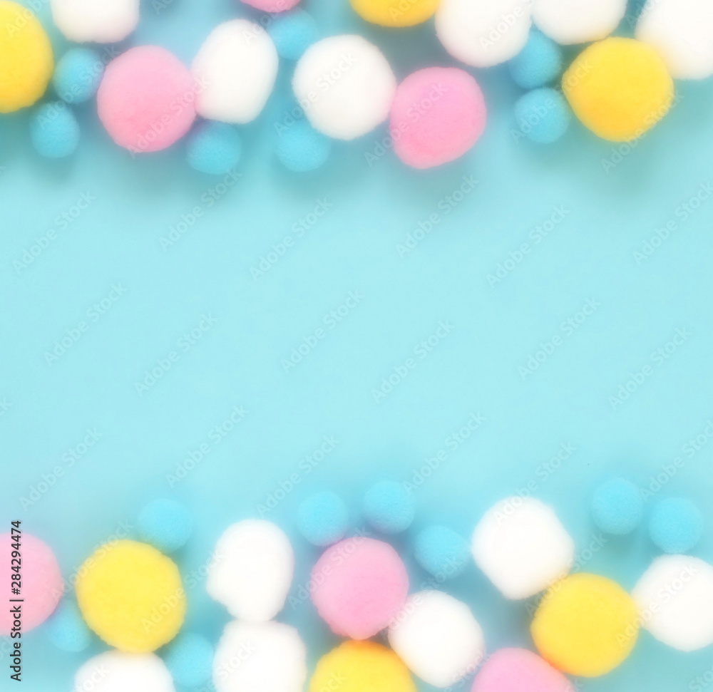 Soft cotton flaffy balls in pastel colors frame on blue background blur effect. Party, birthday, baby shower, invitation concept. Copy space. Top view Soft cotton flaffy balls in pastel colors frame on blue background blur effect. Party, birthday, baby shower, invitation concept. Copy space. Top view