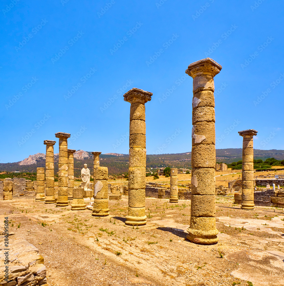 Remains of the main Basilica and the statue of the Roman Emperor Trajan in Baelo Claudia Archaeological Site. Tarifa, Cadiz. Andalusia, Spain.