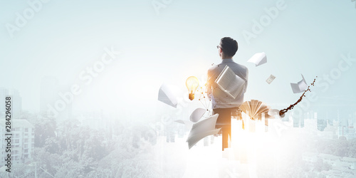 Back view of standing white businessman looking ahead with office objects on cityscape background
