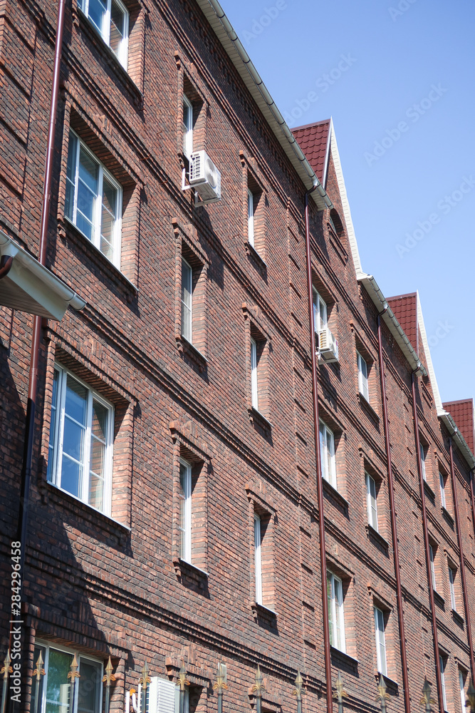 Multi-storey red brick residential building against the blue sky. Summer nature.