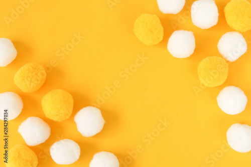 Soft cotton flaffy balls yellow white colors frame on yellow background. Party, birthday, baby shower, invitation concept. Copy space. Top view