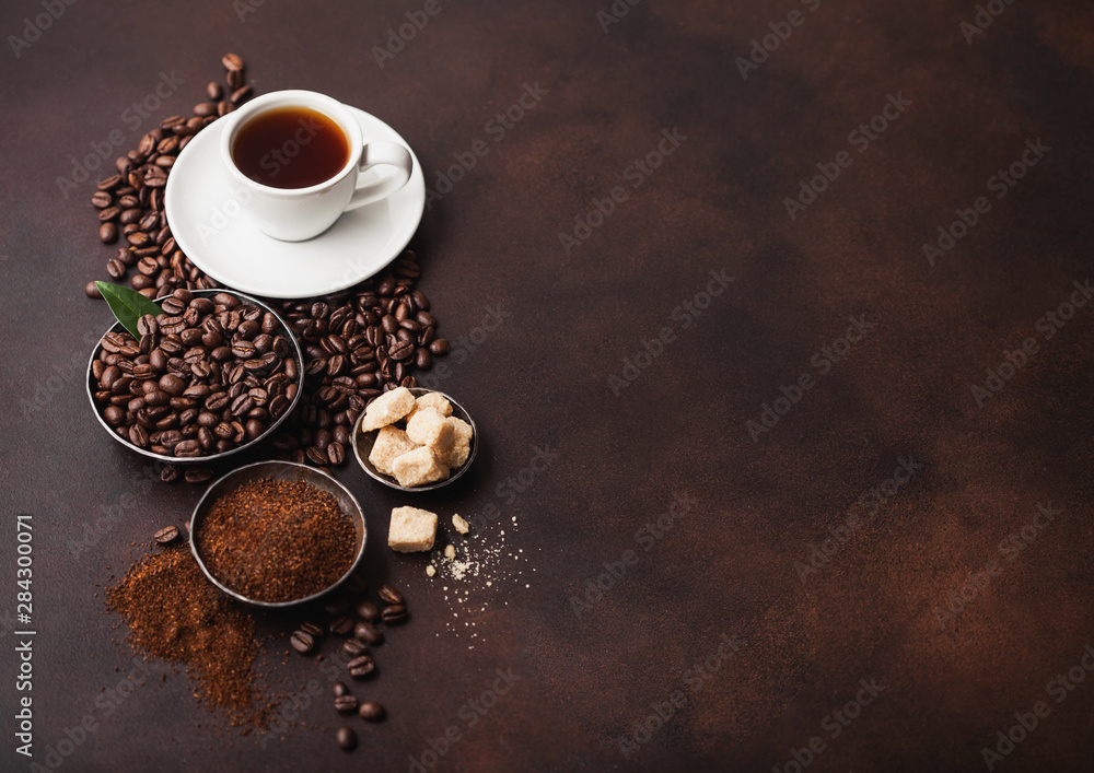 White cup of fresh raw organic coffee with beans and ground powder with cane sugar cubes with coffee tree leaf on brown background. Top view. Space for text White cup of fresh raw organic coffee with beans and ground powder with cane sugar cubes with coffee tree leaf on brown background. Top view. Space for text