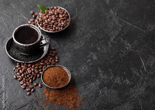 Cup of fresh raw organic coffee with beans and ground powder with coffee tree leaf on black background. Top view