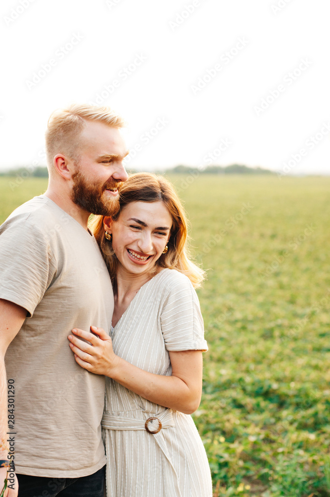 Handsome guy and blonde girl walking on the field on a warm sunset. gently hug, standing in the sun