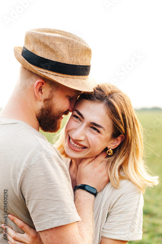 Handsome guy and blonde girl walking on the field on a warm sunset. gently hug, standing in the sun