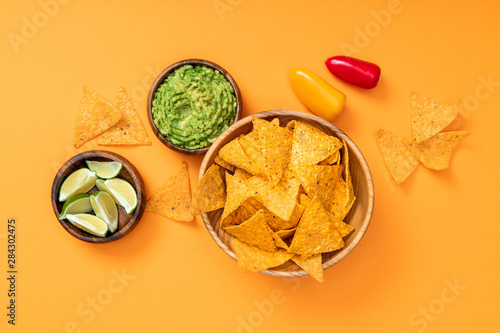 top view of crispy Mexican nachos, guacamole, limes and bell peppers on orange background